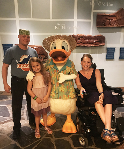 a man in a grass hat and silly smile, a little girl, Donald Duck in a Hawaiian shirt, and a lady in a wheelchair smiling.