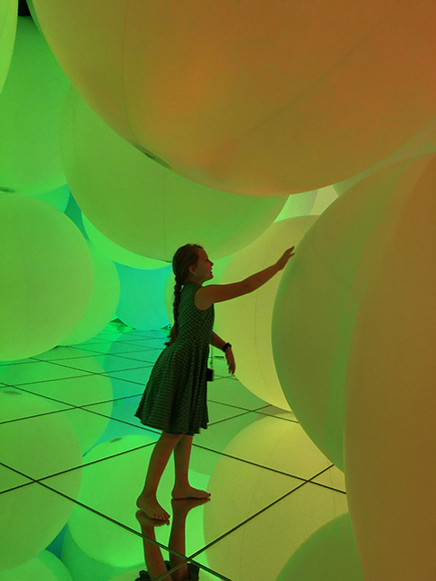 a girl touching a giant green ball in a room of giant green and yellow balls
