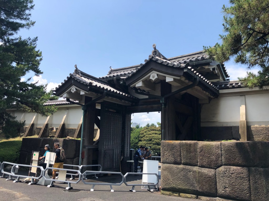 a large feudal Japanese gate with large blocks of stone in a wall to the sides of it
