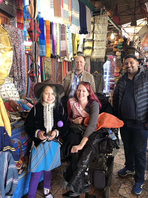 a girl in a hat, two men and a red haired woman in a wheelchair, all smiling.
