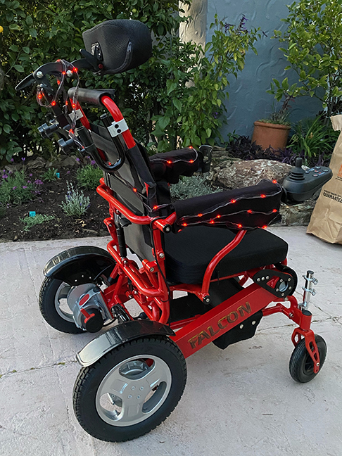 A re wheelchair with red LED lights running along black sleeves on the chair's arms and across the back.