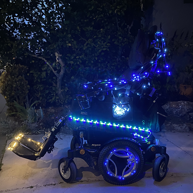A wheelchair in the dark lit with lots of blue and blue/green LED lights.