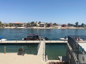 A view of a dock at a river with houses on the opposite bank and boats at the oak