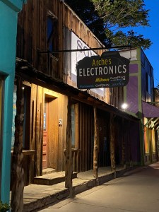 an old wooden beam porch on and old west style building with a sign hanging over it saying “Arches Electronics”