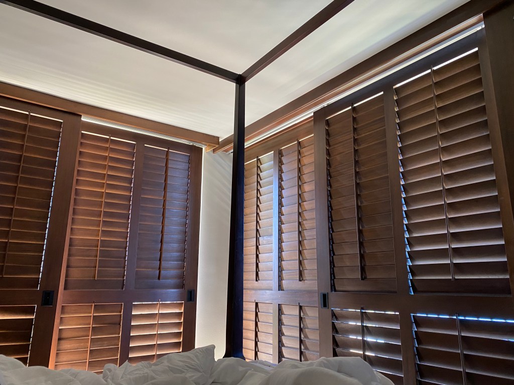 the corner of a room seen from a bed with wooden shutters, all shut