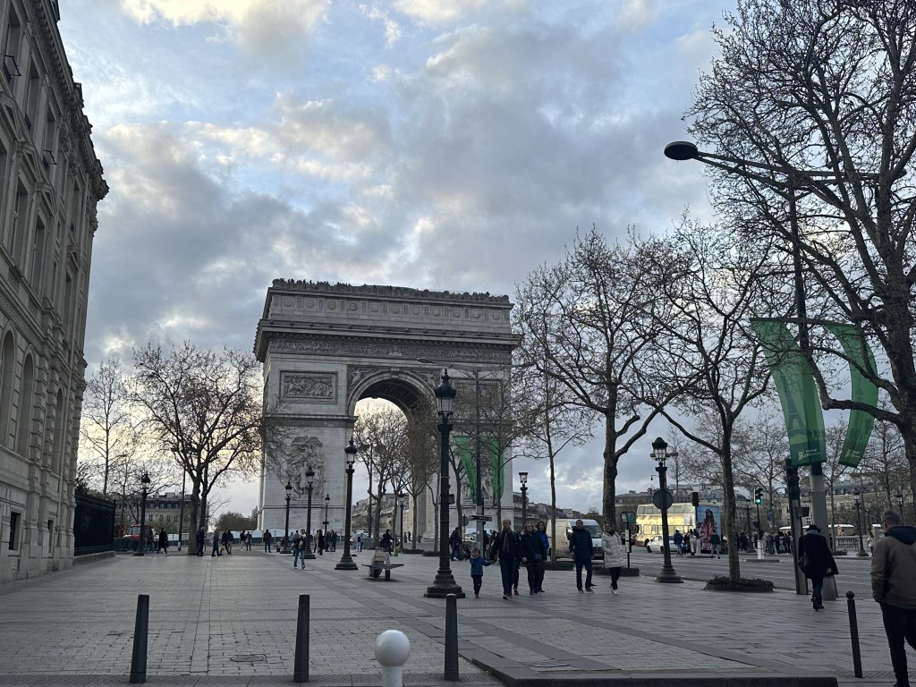 The Arc de Triomphe with people strolling in front of it.  Bare trees.