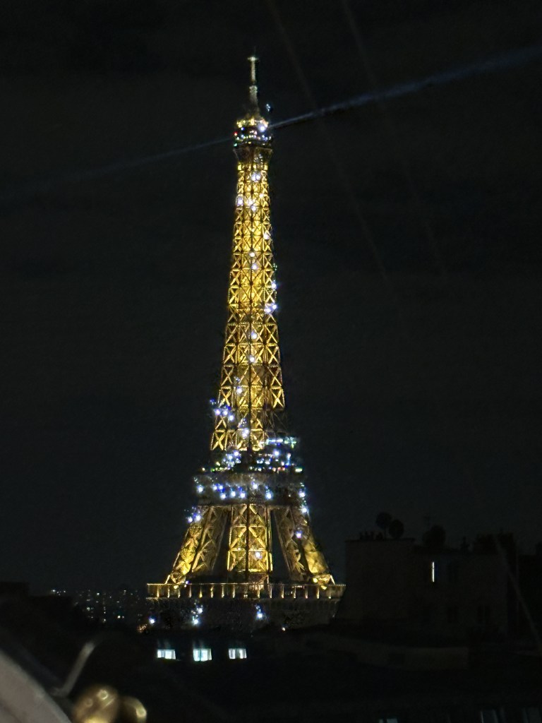 The Eiffel Tower a night, lit with both golden light, and sparkling white lights.