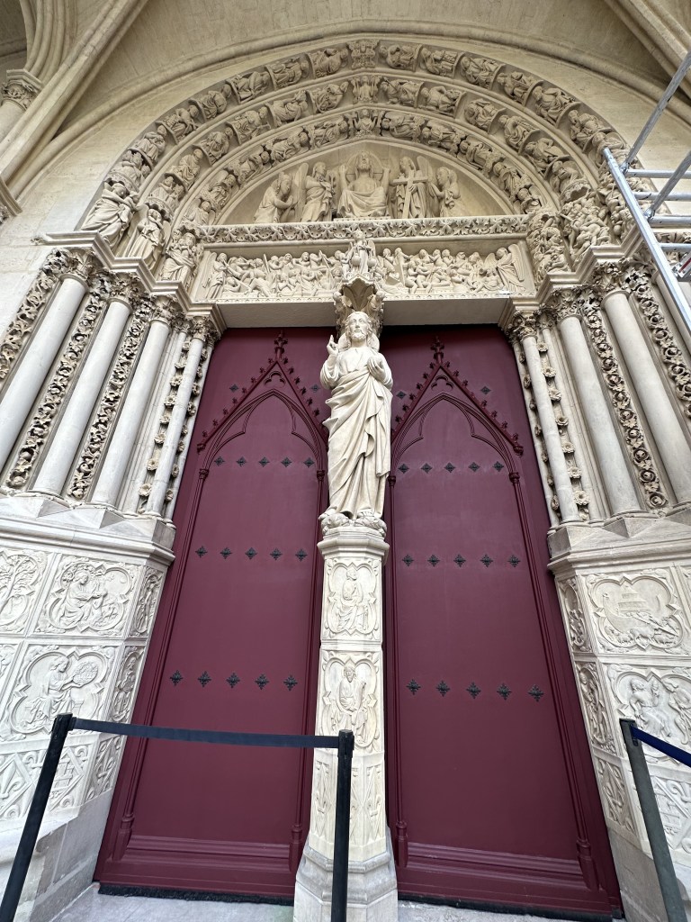 A red double church door with a pillar and figure in the center in white stone.  
