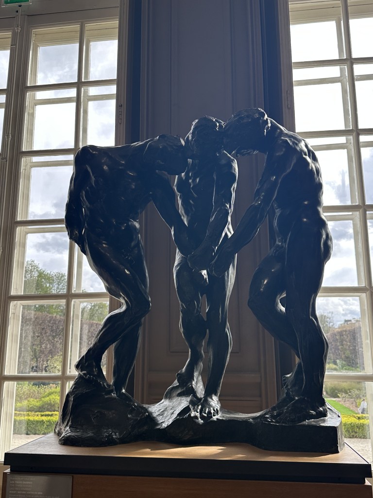 A bronze sculpture of three standing men leaning in and touching hands.