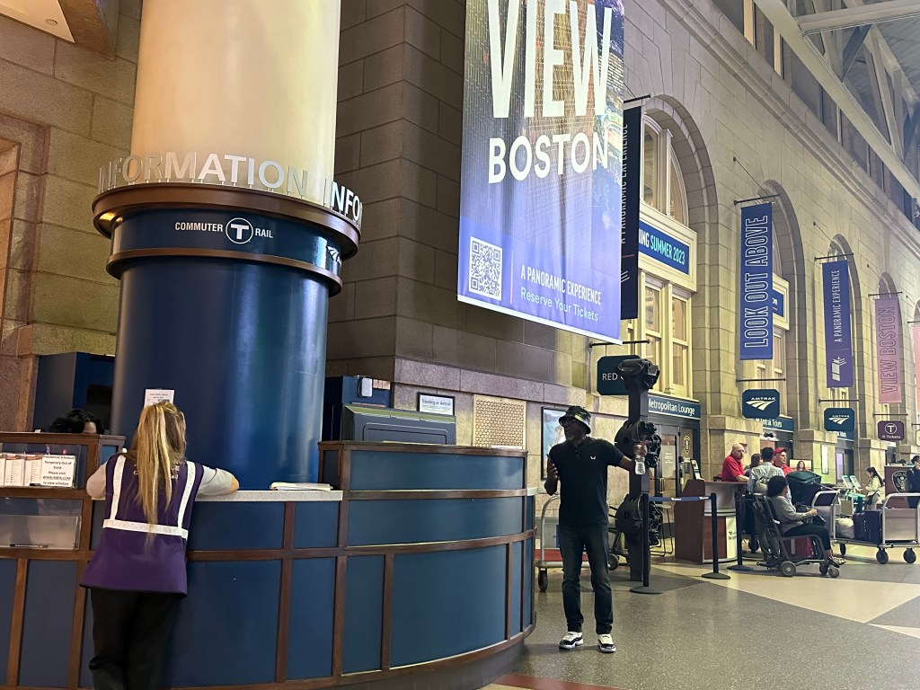 A picture of an information desk (left) with the Amtrak desk in the background (right) with red-jackets employees at the desk.
