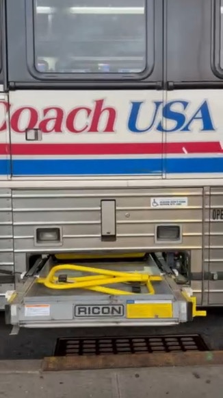 The side of a bus with a partially deployed wheelchair elevator.